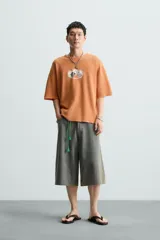 Camiseta boxy fit de punto tejido en hilatura de algodón, color terracota, con cuello redondo y manga corta. Estampado frontal de dados en tonos grises y blancos dentro de un óvalo.