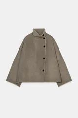 Cazadora de corte amplio confeccionada en hilatura con lana, color beige. Presenta cuello subido, manga larga y cierre frontal con botones negros. Destaca por sus acabados con costuras de hilo a contraste en los bordes.