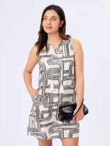Vestido corto de línea A, color blanco con estampado geométrico en negro. Cuenta con diseño sin mangas, escote en V con cordones decorativos terminados en borlas y bolsillos laterales.