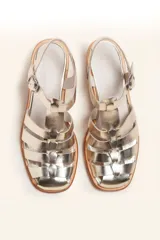 Sandalia plateada de cuero con tiras entrecruzadas, taco de madera y hebilla lateral.