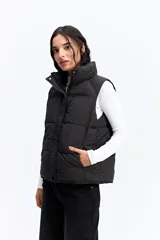 Chaleco puffer negro con cuello alto, cierre frontal y broches a presión. Diseño acolchado liviano con bolsillos laterales.