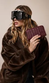 Billetera de dama en símil cuero color negro, de diseño acolchado con costuras verticales que forman relieves y cierre perimetral. Incluye monograma en la esquina inferior y viene con caja de presentación estampada.