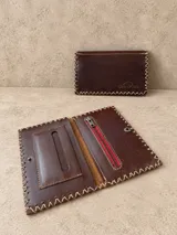 Billetera y tabaquera de cuero marrón con costuras decorativas artesanales en el contorno y cierre con botón a presión. Cuenta con compartimentos interiores para accesorios y tarjetas.