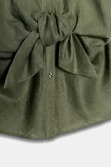 Camisa blanca confeccionada en tejido con lino, con cuello solapa y manga muy corta con terminación en vuelta. Presenta un detalle de nudo en el delantero y cierre frontal con botones metálicos.