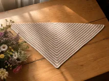 Chal pañuelo de formato triangular tejido a mano en lana merino y seda, con diseño de rayas diagonales en tonos beige y marrón.