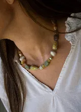 Collar corto compuesto por cuentas y piedras artesanales en tonos verdes, amarillos, beige y marrones, de diseño único.