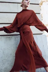 Vestido largo fluido en color bordó, confeccionado en georgette. Presenta cuello redondo, mangas largas con pliegues terminadas en puños y tiras ajustables para atar en la cintura. Incluye forro interior a tono.