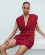 Vestido corto rojo con escote en V cruzado, sin mangas y con detalle drapeado en la falda.