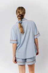 Pijama de algodón color celeste, compuesto por una camisa de manga corta con botones marrones y ribetes festoneados en color marrón, y un short con elástico en la cintura y ribetes festoneados en el ruedo.