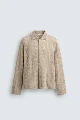 Sobrecamisa de hombre color beige, confeccionada en tejido de crochet con estructura abierta, cuello solapa, manga larga y cierre frontal de botones.