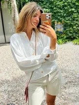 Camisa de lino blanca, de corte oversize, con mangas largas abullonadas, cuello mao y botones. Es más larga en la parte trasera e incluye un tajo en la espalda.