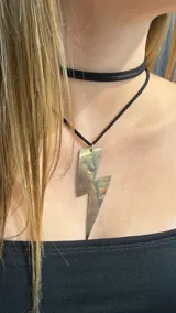 Choker doble compuesto por una gargantilla de gamuza negra y un collar largo con dije metálico en forma de rayo.