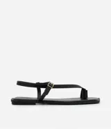 Sandalias planas de cuero sintético negro, con puntera cuadrada, tira delantera con dedera y tira trasera con hebilla metálica dorada.