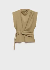 Blusa sin mangas color beige con cuello perkins y hombreras marcadas. Presenta un diseño recto con cinturón ajustable integrado en la cintura y cierre de cremallera en la parte posterior.