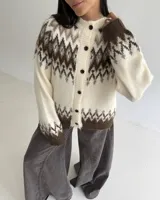 Cardigan de punto con diseño jacquard de inspiración nórdica, en tonos blanco, gris y marrón. Presenta cuello redondo, cierre frontal con botones y mangas largas con puños acanalados.