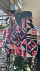 Chaleco marrón con estampado abstracto en tonos marrones y negros, con cierre frontal y broches a presión. Interior forrado con tela de peluche color crema y bolsillo interno.