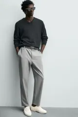 Pantalón de corte slim fit y color negro, confeccionado en tejido elástico. Cuenta con cintura elástica, trabillas, bolsillos frontales y cierre con cremallera y botón.