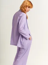 Blazer oversized lila de corte recto, largo a la cadera, con hombreras finas forradas, costuras internas con sesgo combinado y maxi bolsillos delanteros. Incluye lazo de algodón con detalle a tono.
