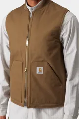 Chaleco de trabajo Carhartt WIP, color azul marino, con cierre frontal completo, cuello tipo bomber y bolsillos delanteros. Presenta el logo de la marca bordado en el pecho.