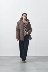 Campera puffer negra con diseño acolchado, capucha integrada y cierre frontal con botones a presión. Presenta puños elásticos y costuras decorativas en el frente.