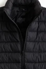 Chaleco acolchado de nylon rompevientos, color negro, con diseño guateado, cuello elevado y cierre frontal. Cuenta con bolsillos laterales con cierre y forro interior.