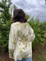 Buzo amplio de frisa liviana de algodón color gris con estampado botánico de hojas en tonos verdes. Tiene cuello redondo y tajos laterales.