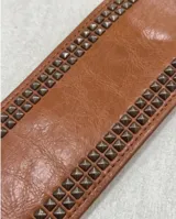 Cinto tipo faja color marrón con múltiples filas de tachas metálicas y hebilla frontal con argolla.