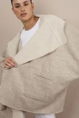 Ruana color crudo de lana fina sin teñir, con capucha, bolsillos y terminaciones envivadas. Tiene un broche para usar cerrada. Es una prenda oversize sin forro, cómoda, versátil y fácil de combinar.
