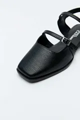 Sandalias chatitas Daniel Cassin color negro con textura símil reptil, punta cuadrada, taco bajo y doble tira delgada con hebilla metálica.