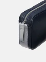 Cartera tipo camera bag de Calvin Klein, color azul marino oscuro, con textura de cuero granulado. Presenta un logo CK grabado en bajo relieve en el frente y una correa ajustable de tela gris claro.