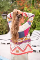 Sweater de punto con diseño geométrico multicolor y cuello redondo. El borde del cuello, puños y ruedo es de color salmón fluorescente.