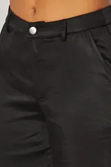 Pantalón de vestir de corte recto confeccionado en satén negro, con cintura de tiro alto, cierre frontal con botón y bolsillos laterales.