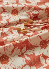 Mono largo de tejido fluido con estampado floral en tonos naranja y blanco. Diseño con tirantes finos y detalle fruncido en la cintura.