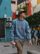 Sudadera celeste con cuello redondo, puños y cintura acanalados. Estampado frontal con la palabra "Zurich" en letras plateadas.