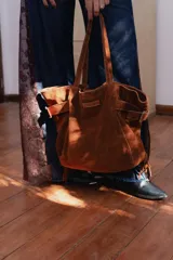 Bolso tipo shopper confeccionado en cuero descarne color marrón, con diseño de flecos en los laterales y correas ajustables con hebillas metálicas. Incluye doble bolsillo interno y tira porta llaves.