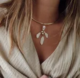 Gargantilla rígida dorada con dije colgante con forma de flor, adornado con perlas y piezas de nácar.