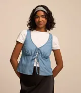 Blusa sin mangas confeccionada en jeans celeste, con escote V, recorte en el busto, fruncido y lazo con lacitos delanteros.