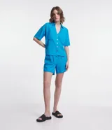 Camisa de manga corta confeccionada en mezcla de viscosa y lino color turquesa. Presenta cuello camisero con escote en V, bolsillos frontales de parche y cierre frontal con botones geométricos de efecto carey.