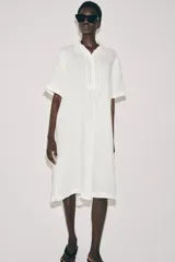 Vestido camisero de lino con cuello solapa, manga corta y cierre frontal con botones. Presenta un diseño con bajo redondeado y aberturas laterales.