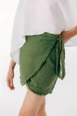 Minifalda verde oliva de lino con corte irregular y lazo lateral. Presenta detalle de flecos en el ruedo.