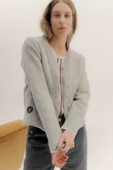 Saco tejido de lana con diseño de ochos y aranes en el frente. Presenta cierre frontal con ganchos peleteros, cuello redondo y pin bordado de la marca en la parte inferior.