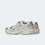 Championes Asics modelo Gel 1130, color blanco y plateado con detalles en negro, confeccionados con malla transpirable y revestimientos sintéticos, inspirados en el diseño de running de 2008 y equipados con tecnología GEL en el talón.
