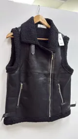 Chaleco de cuero sintético marrón con interior y detalles de corderito sintético en cuello y bordes. Cuenta con cierre frontal cruzado, bolsillos con cierre y hebillas laterales ajustables.