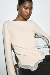 Top de manga larga en tejido suave color gris, con cuello redondo y bajo asimétrico decorado con encaje negro a tono. Presenta detalles de encaje negro en los puños.