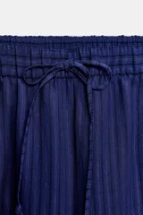 Pantalón de tiro medio con diseño de pierna ancha y textura acanalada. Cuenta con cintura elástica ajustable mediante cordones.