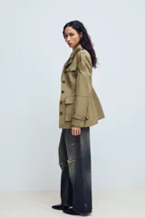 Chaqueta de estilo militar en color beige, con cuello subido, cierre frontal de botones, bolsillos de plastrón con solapa en el frente y detalle de hombreras con trabillas.