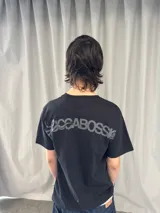 Remera de algodón color negro con estampado serigráfico en tono gris oscuro en la parte posterior. Presenta cuello reforzado, costuras reforzadas y una pequeña etiqueta decorativa en la manga.