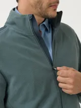 Campera polar RKF modelo Volterra color verde grisáceo, con cierre frontal completo, cuello alto y mangas largas. Presenta aplicaciones de tela canvas de algodón en los hombros, dos bolsillos frontales con cierre y bolsillos internos. Confeccionada en poliéster reciclado.