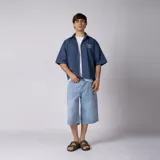 Camisa de manga corta azul oscuro de corte boxy, confeccionada en algodón. Presenta cuello camisero, cierre frontal con botones y un pequeño bordado en el pecho con las siglas 'VCP CNPT' y el número '333'.