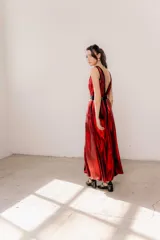 Vestido largo de seda color bronce con acabado brillante, escote profundo en V y espalda abierta. Presenta detalles en terciopelo negro que enmarcan el escote, recorren el frente y definen la cintura con una faja ajustable. Posee breteles anchos y una abertura frontal en la falda.